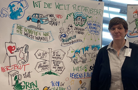 Autorin steht vor einem Bild mit dem graphic recording eines Konferenz-Workshops